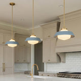 A transitional kitchen features three Blaine Medium Pendant 16", Brass and French Blue with brushed brass rods over a marble island and beige cabinetry with subway tile.