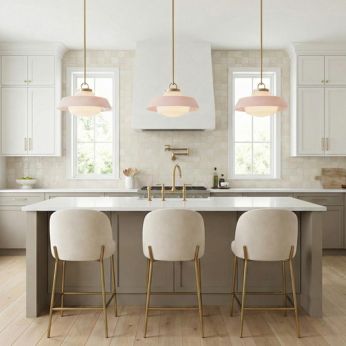 A transitional kitchen features three Blaine Medium Pendants 16 inch Brass and Rose Quartz suspended over a white quartz island with cream stools and tiled backsplash.