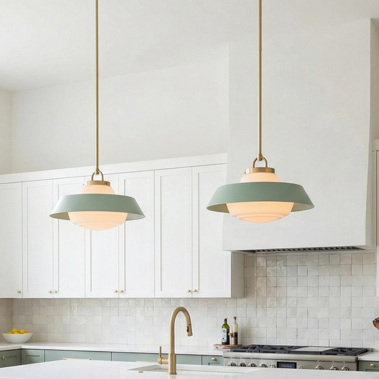 A contemporary kitchen featuring two Blaine Medium Pendant 16", Brass and Sage Green fixtures with frosted glass hanging over a white island set against white shaker cabinets.