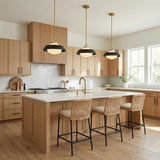 A contemporary kitchen features three Blaine Medium Pendant 16", Brass and Matte Black fixtures with frosted glass shades over a white quartz island and light wood cabinets.