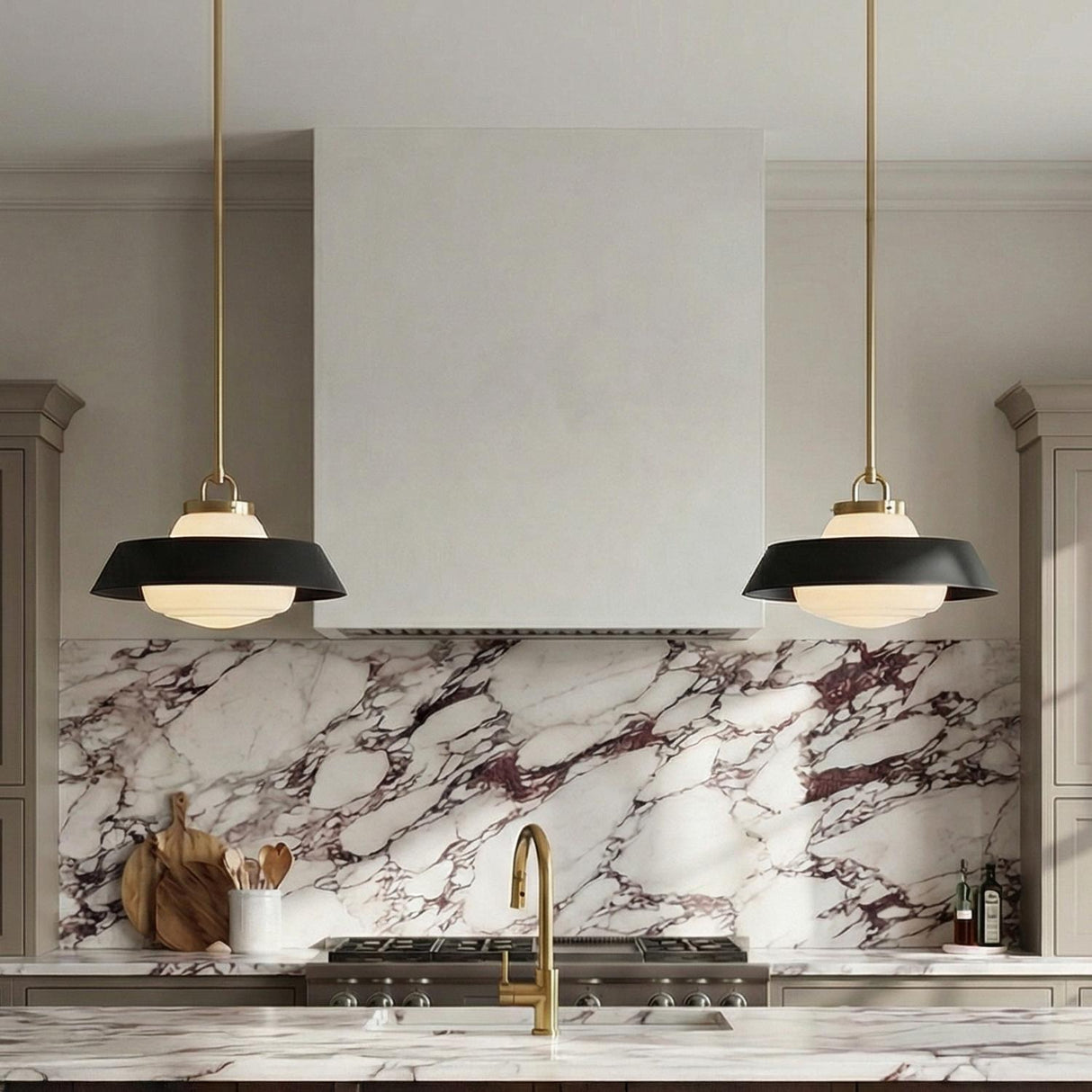 A contemporary kitchen features two Blaine Medium Pendant 16", Brass and Matte Black fixtures flanking a white range hood above a purple-veined marble backsplash.