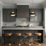 A transitional kitchen features two Blaine Large Pendant 20 inch Brass and Matte Black pendants with frosted glass over a gray island with brass leather barstools.