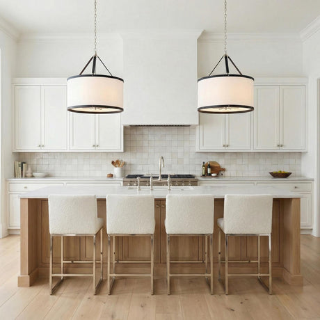 A transitional kitchen features two Spencer Pendant 28-inch Polished Nickel with Black Leather Accents drum pendants with linen shades suspended over a natural wood island.