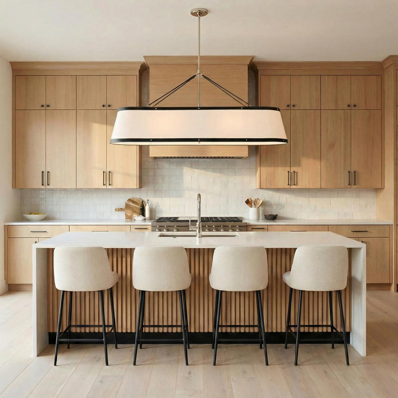 A transitional kitchen features the Spencer Linear Pendant, Polished Nickel with Black Leather Accents over a white waterfall island with fluted wood detailing and light wood cabinetry.