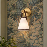 A transitional foyer features the Spencer Wall Sconce 14", Brass with Brown Leather Accents mounted against a detailed forest tapestry wallpaper beside green foliage.