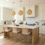 A transitional kitchen features three Florence Pendant 13", Soft Brass globe pendants over a white marble island with light wood cabinets and rattan counter stools.