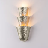 Hammered metal wall sconce with warm glow on a light gray background