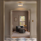 A traditional foyer with the Pippa Flush Mount 12", Aged Brass and Rustic White along the ceiling over checkered marble tile and a grey velvet armchair.