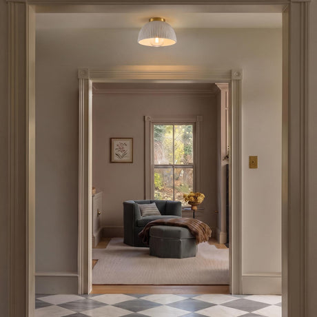 A traditional foyer with the Pippa Flush Mount 12", Aged Brass and Rustic White along the ceiling over checkered marble tile and a grey velvet armchair.