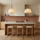 A contemporary kitchen features two Winthrop Fabric Pendant, Medium, 20", Patina Brass and Wood fixtures over the island with a terracotta patterned backsplash and wood cabinets.