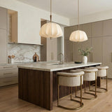 A contemporary kitchen features two Winthrop Fabric Pendant, Medium, 20", Patina Brass and Wood fixtures with linen shades over a fluted wood island and marble backsplash.