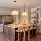 A transitional kitchen with two Winthrop Fabric Pendants in patina brass and wood over a marble island with woven bar stools and a patterned tile backsplash.