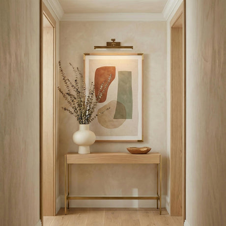 Roland LED Picture Light 16", Patina Brass linear wall sconce in a Contemporary Hallway with a light wood console and abstract art.