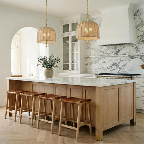 A transitional kitchen features two Benito Medium Pendant 15" Gold Leaf and Natural Rope fixtures over a white marble island with woven leather barstools.
