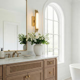 Empire LED Aged Brass linear wall sconce in a Transitional Bathroom with a ribbed wood vanity and marble countertop.