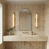 Empire LED Wall Sconce 28", Aged Brass linear Wall Sconce in a Traditional Bathroom with floral wallpaper and a fluted vanity.