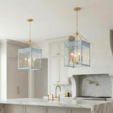 A transitional kitchen features two light blue and aged brass lantern pendants suspended over a white marble island with a herringbone tile backsplash and brass pot filler.