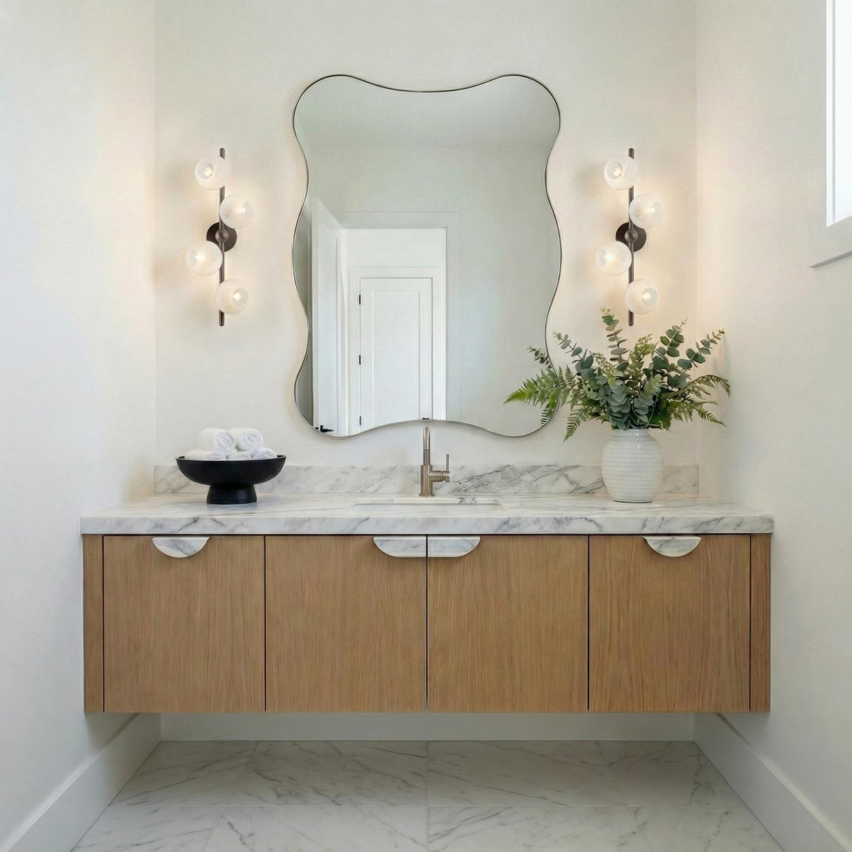 Felix 4 Light Wall Sconce 28", Bronze Leaf and Seeded Cloud Glass Bronze globe Wall Sconce in a Contemporary Bathroom with a wavy mirror.