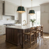 A transitional kitchen features two Avery 4 Light Large Pendants in forest green and aged brass over a marble island with dark wood cabinets and woven stools.