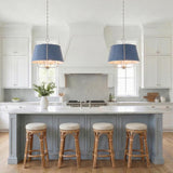 A transitional kitchen features two Avery 6 Light Extra Large Pendants in Dutch Blue and polished nickel over a marble island with rattan stools and gray herringbone backsplash.