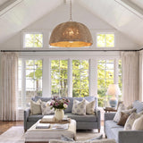 A coastal living room with a Santiago Extra Large Pendant in natural rattan and patina brass hanging from a vaulted shiplap ceiling above soft blue sofas.