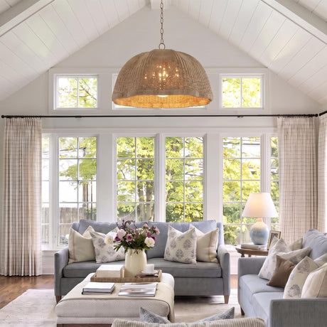 A coastal living room with a Santiago Extra Large Pendant in natural rattan and patina brass hanging from a vaulted shiplap ceiling above soft blue sofas.
