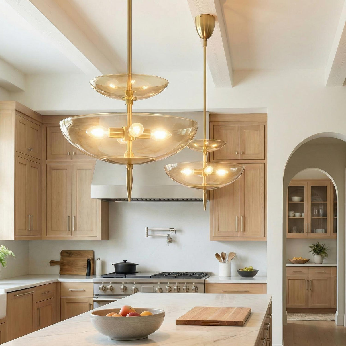 A transitional kitchen features two Zara Large Two-Tier Pendant 21 inch fixtures in brushed brass and chamomile glass over a marble island under a white beamed ceiling.