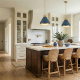 A transitional kitchen features two Drew Medium Pendant 19" Vintage Blue and Aged Brass fixtures over a marble island with dark wood cabinets and woven rattan stools.