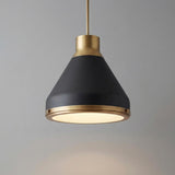 A modern kitchen features the Drew Medium Pendant 19", Matte Black and Aged Brass hanging over an island against a simple gray wall with a frosted glass diffuser.