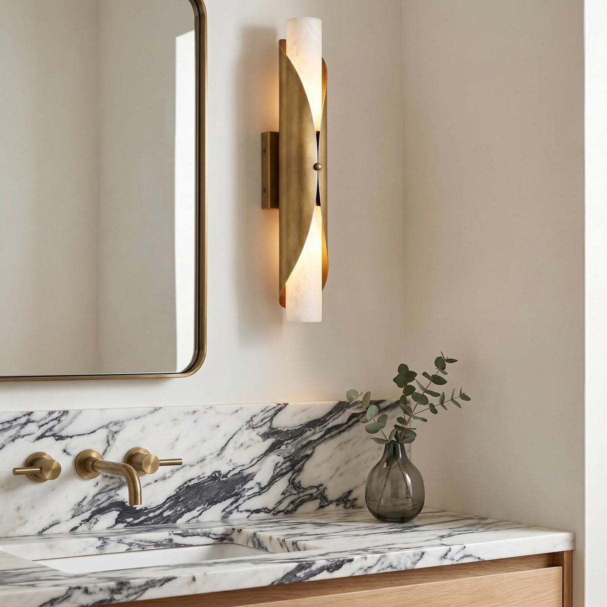 A contemporary bathroom with an Alessio Large Wall Sconce 24", Distressed Brass and Alabaster, mounted beside a mirror over a white marble backsplash and brass faucet.