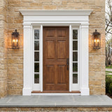 A Colonial entry featuring two Trevor Outdoor Wall Light, Medium 20", Bronze fixtures flanking a wood front door on a stone wall with white trim at dusk.