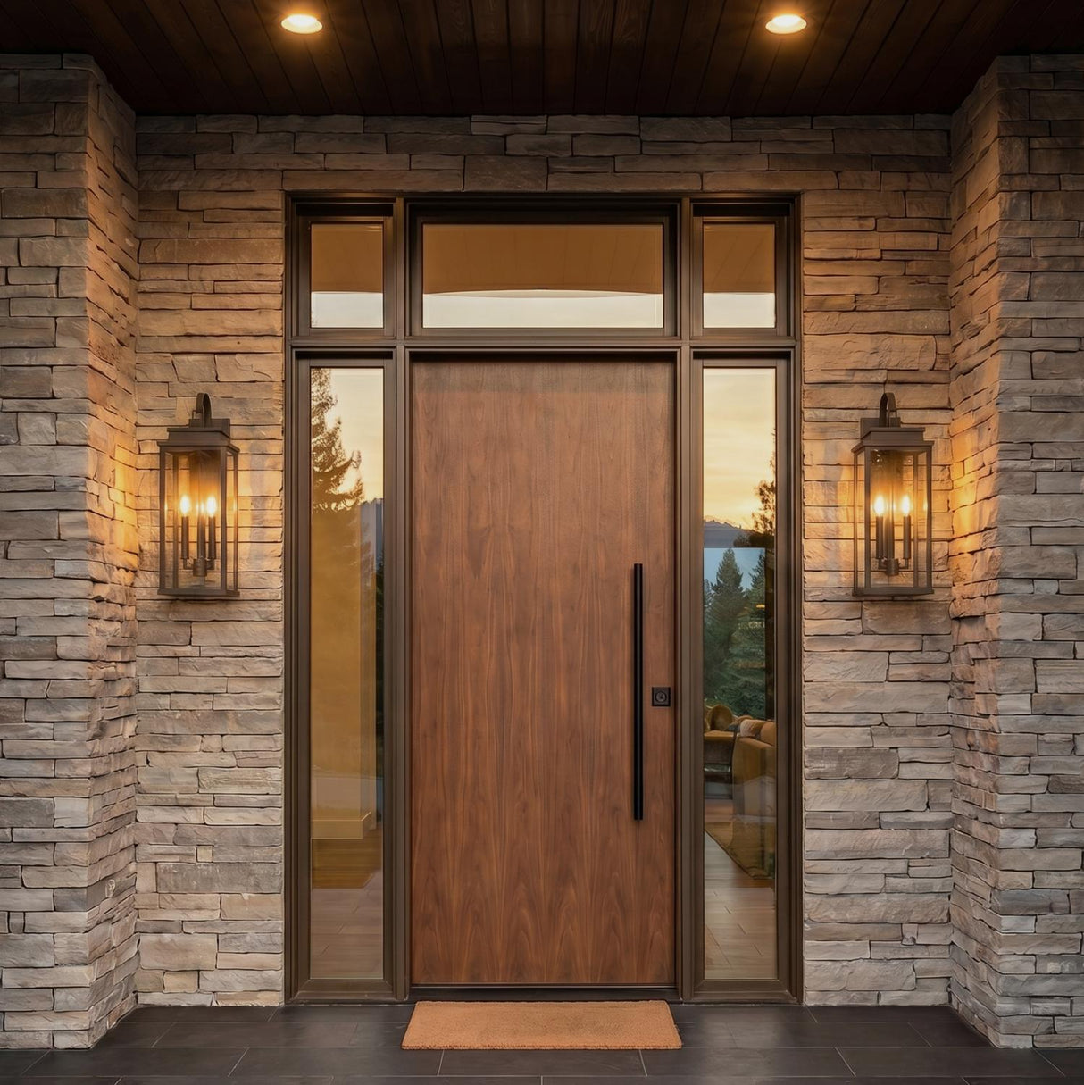 A modern home entry with two oiled bronze Trevor Outdoor Wall Light lanterns flanking a wood front door on a stacked stone facade at twilight.