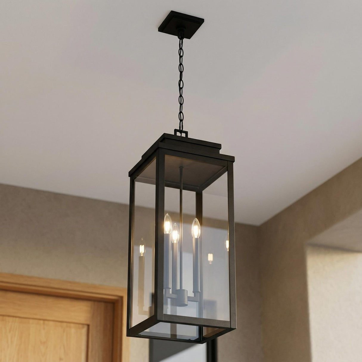 A modern entryway with the matte black Trevor Outdoor Hanging Light, Extra Large 28", Black lantern featuring clear glass panels over the wood door entry.