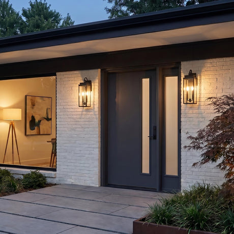 A modern entryway with two matte black Trevor Outdoor Wall Light lanterns flanking a charcoal gray front door set into a white brick wall.