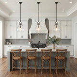A transitional kitchen featuring three Naya Medium Pendant 12", Matte Black and Clear Glass fixtures over the island with wooden stools under a coffered ceiling.