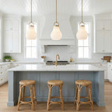 A farmhouse kitchen featuring three Naya Medium Pendant 12", Satin Brass and Opal Glass fixtures over a marble island with blue-gray cabinets and woven rattan stools.
