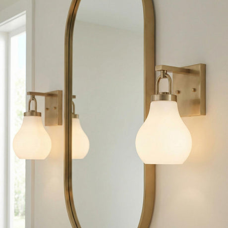 Naya Vanity Wall Sconce, Satin Brass and Opal Glass geometric Wall Sconce in a Contemporary Bathroom with an oval brass mirror.