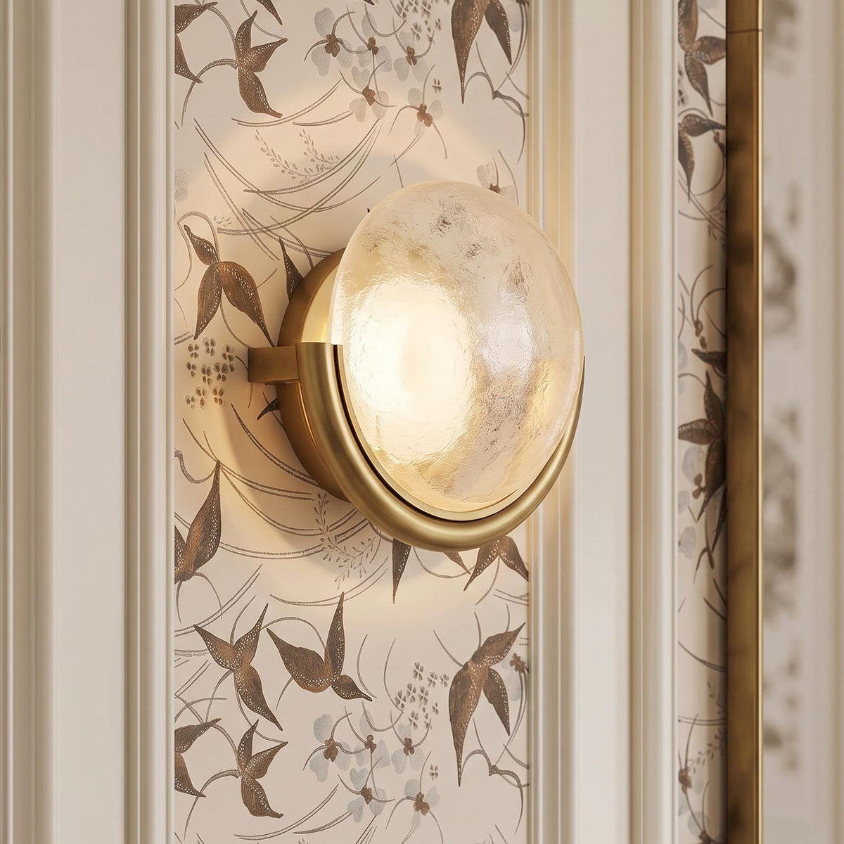 A transitional foyer with a Soleil LED Wall Sconce 11", Antique Brass featuring textured glass mounted on a wall with floral wallpaper and white molding.