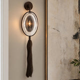 A transitional living room features the Umbria Wall Sconce 37", Bronze with an oval glass shade and dark tassel mounted beside framed abstract artwork.