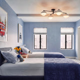 A modern bedroom featuring the Hanley 4 Light Flush Mount in matte black and ivory crackle ceramic centered above twin beds with blue grid wallpaper.