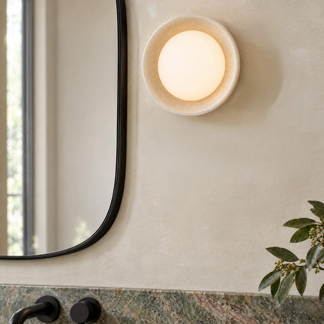 A modern bathroom with a Hanley Wall Sconce in ivory crackle ceramic mounted beside a rounded black mirror above a green marble vanity.