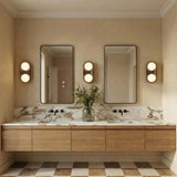 A contemporary bathroom featuring three matte black ceramic Hanley wall sconces with brass accents flanking two mirrors above a veined marble countertop and floating wood vanity.