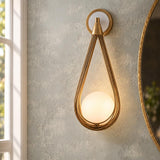 A contemporary bathroom features the Lorien Wall Sconce 21", Antique Brass and Opal Glass mounted on a textured wall beside a round brass mirror.