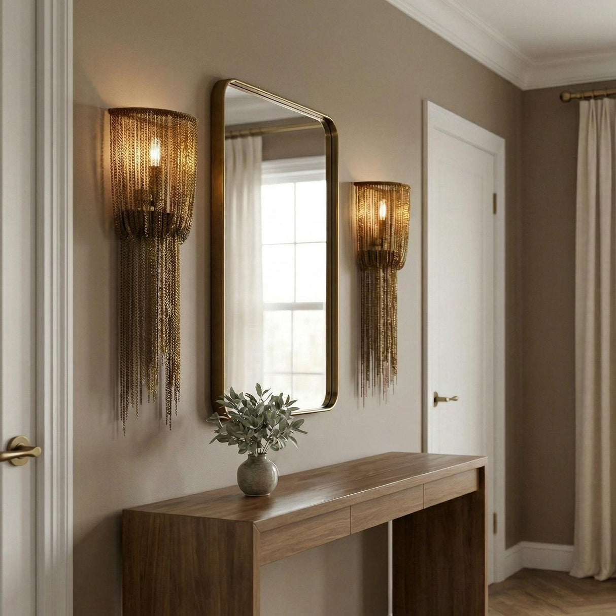 A contemporary entryway with two Talon Large Wall Sconce 24 in antique burnished brass featuring draped chains flanking a gold mirror above a walnut console table.
