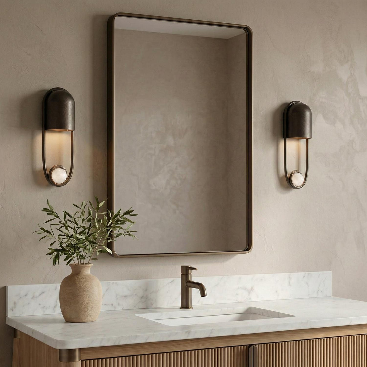 A contemporary bathroom featuring two Bastion wall sconces in English bronze with marble accents flanking a bronze-framed mirror over a white marble countertop.
