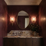A contemporary bathroom featuring the Nadine Wall Sconce in gold and clear seeded glass flanking an organic mirror above a purple-veined marble vanity and dark wood cabinets.