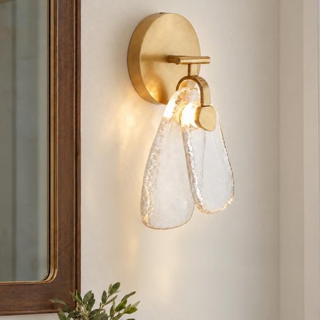 A modern bathroom featuring the Renata LED Wall Sconce 14", Antique Brass and Textured Clear Glass mounted on a wall beside a dark wood-framed mirror.
