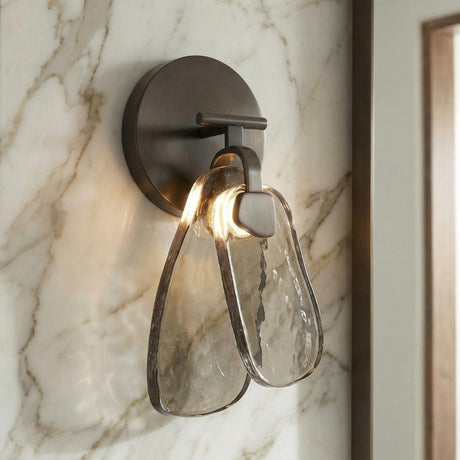 A contemporary bathroom featuring an English bronze wall sconce with textured smoke glass panels mounted on a white and gray veined marble wall near a vanity.