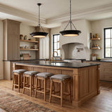 A modern farmhouse kitchen featuring two matte black saucer pendants over a natural wood island with black countertops and a white plaster range hood.