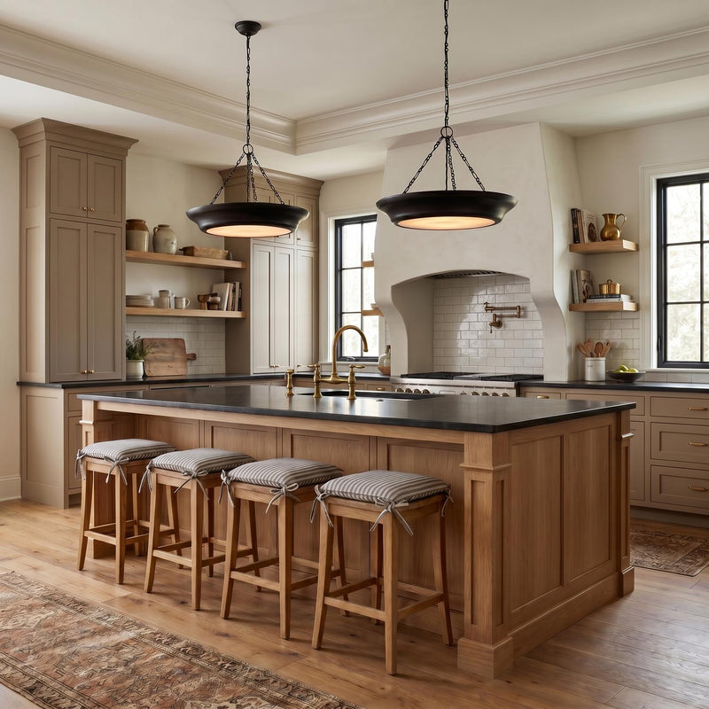 A modern farmhouse kitchen featuring two matte black saucer pendants over a natural wood island with black countertops and a white plaster range hood.